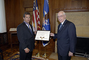 two men standing in a room, smiling at the camera, and holding a Medal of Valor award plaque between them